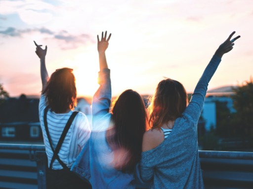 Three young women stretch their arms up in the sunset